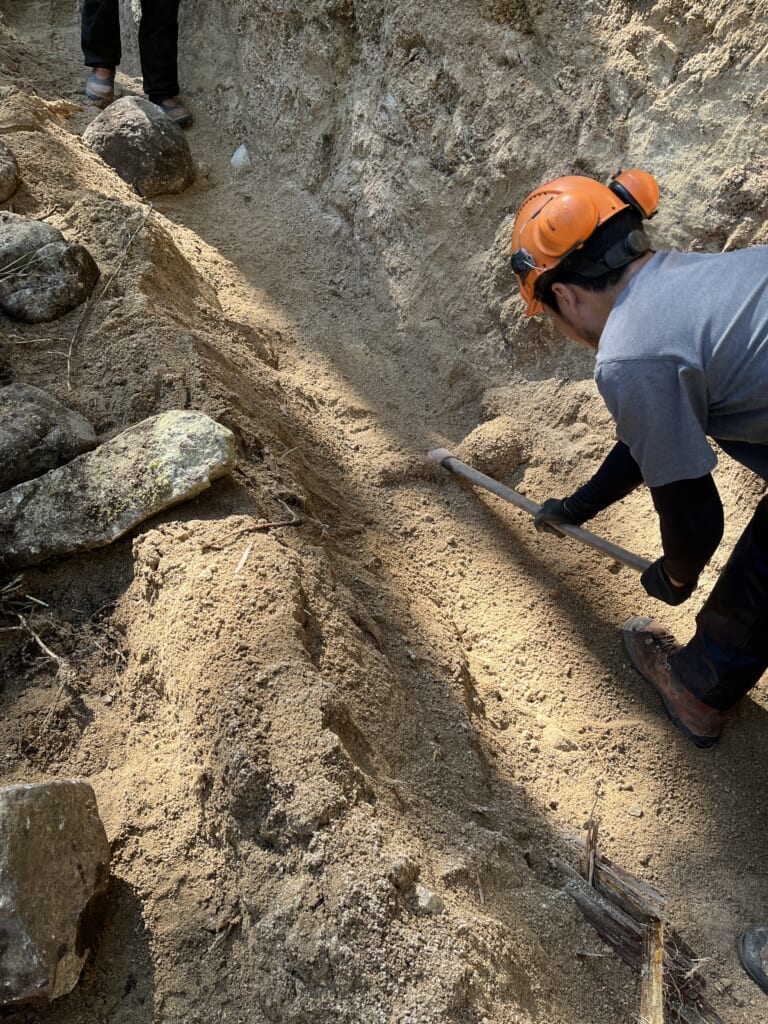 切土の根元で、作業者が手工具を使って床掘り箇所の土を整えている様子